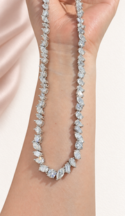 Close view of Eveline's mixed-shape moissanite necklace against warm paper and blush silk.