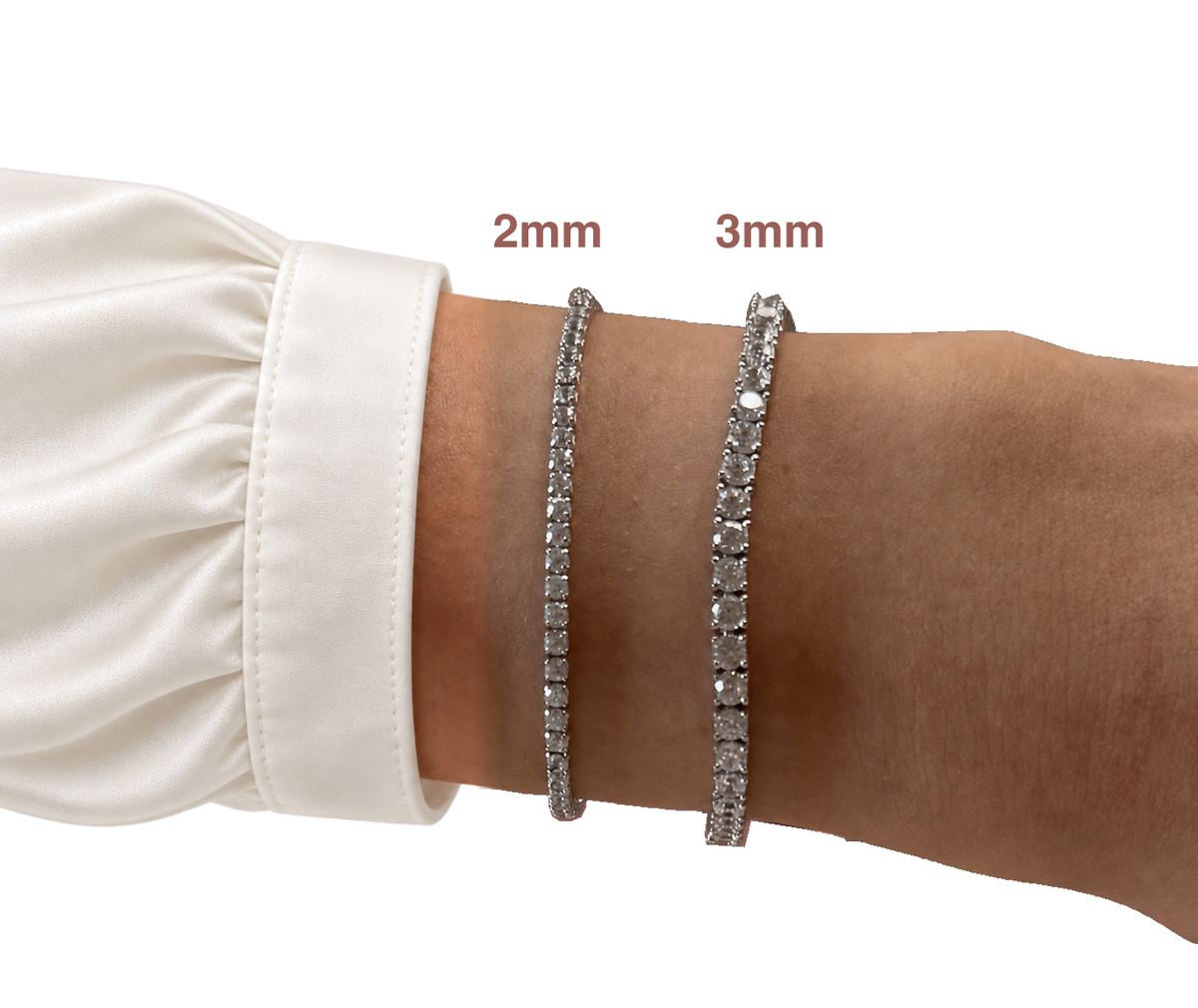 Two Eira Current tennis bracelets worn on a wrist beside an off-white silk blouse cuff on white, with small 2mm and 3mm width labels.