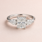 Lumera Passage radiant-centre ring with pear side stones — existing silver-tone design illustration, used temporarily; not a photograph of the finished silver and moissanite edition.