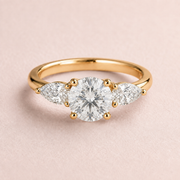 Lumera Passage three-stone ring concept with a round brilliant centre and pear-shaped side stones in yellow gold