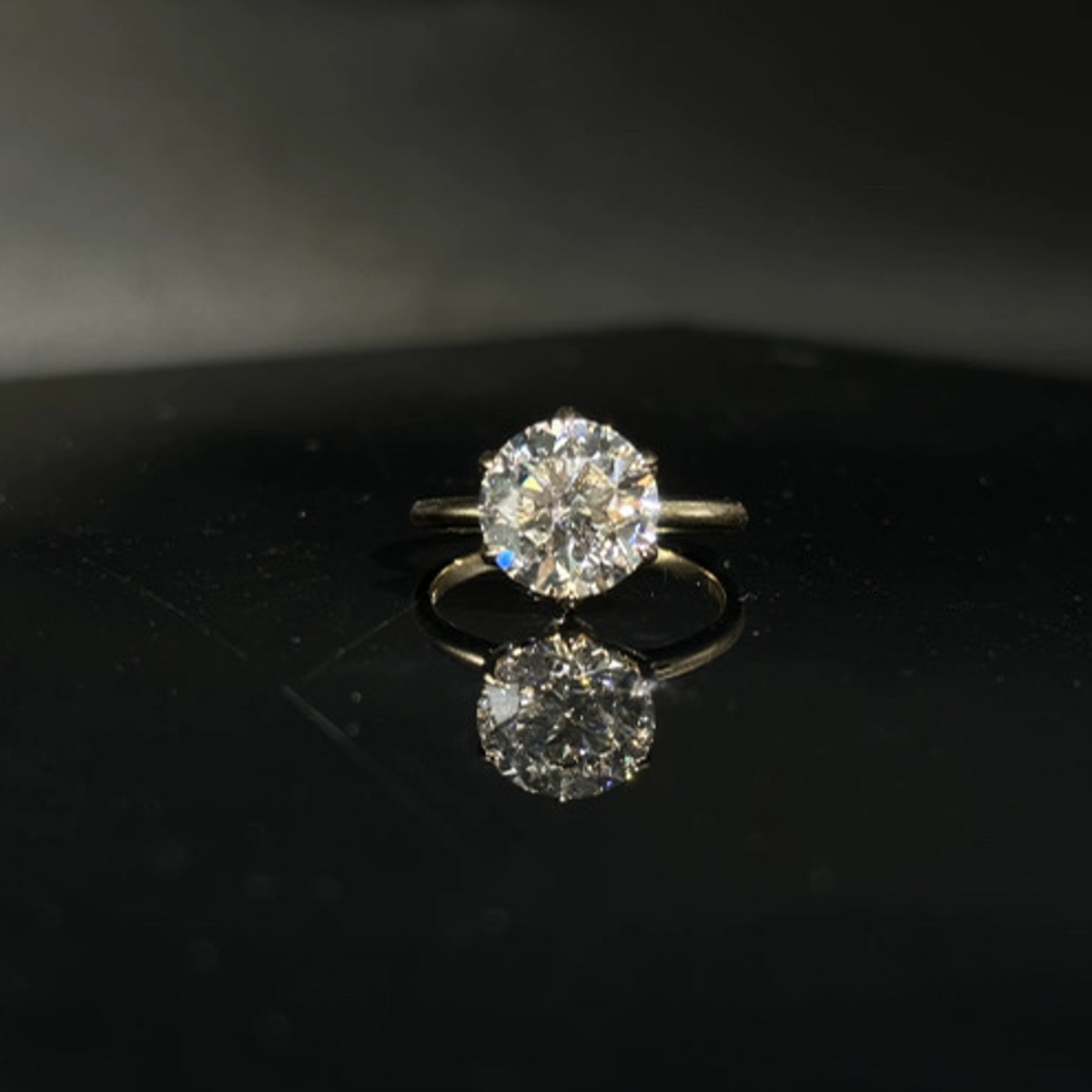 Olivia's Ovation round brilliant lab-grown diamond ring viewed from the front on polished black Perspex