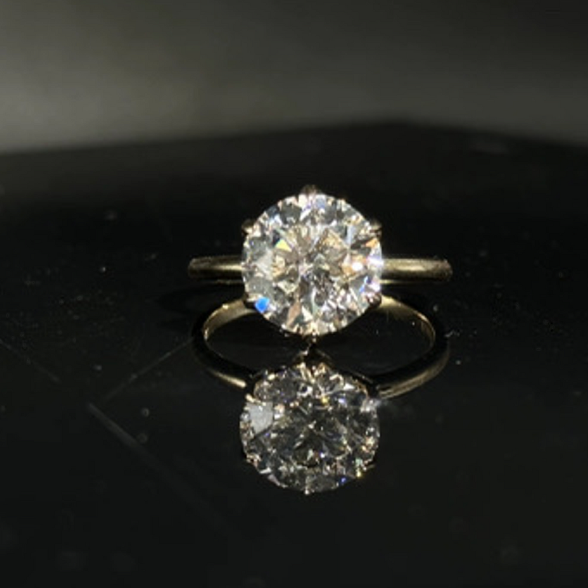 Olivia's Ovation round brilliant lab-grown diamond ring, centred front view on polished black Perspex